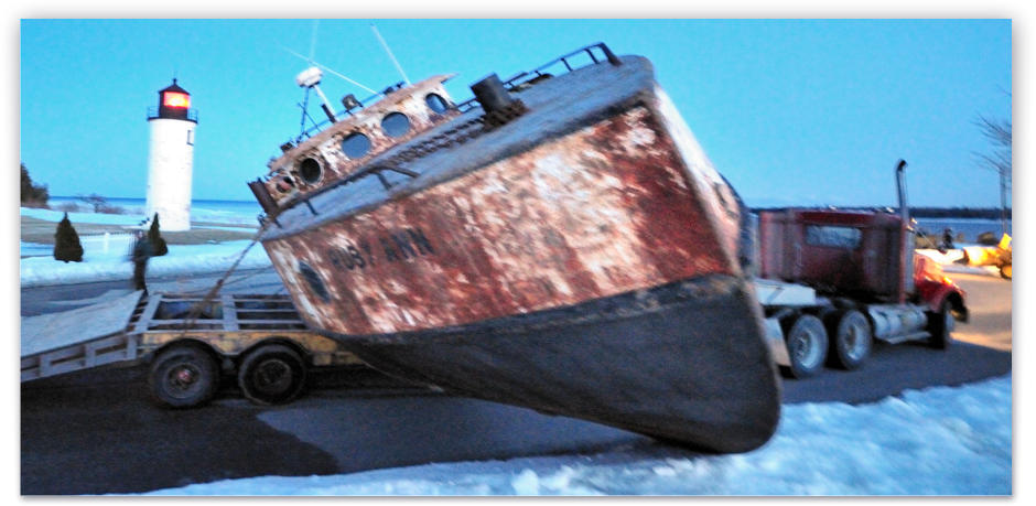 Passing the Whiskey Point Lighthouse, on a trailer, the Ruby Ann approaches her winter launch spot at the point